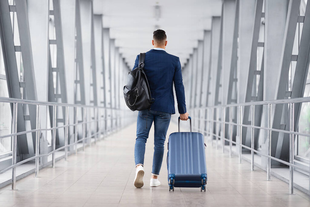 Hombre con ropa casual caminando con equipaje en la terminal del aeropuerto, vista trasera - Foto, imagen