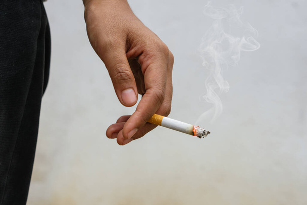 Woman holding smoking a cigarette in hand. Cigarette smoke spread. - Фото, зображення