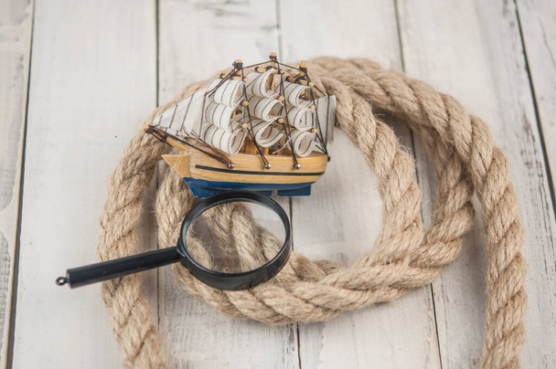 麻ロープ、虫眼鏡と古い白い木の背景にモデルの古典的なボート  - 写真・画像