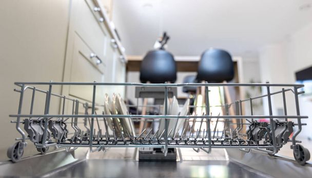 Open dishwasher with clean dishes on blurred kitchen background. - Photo, Image
