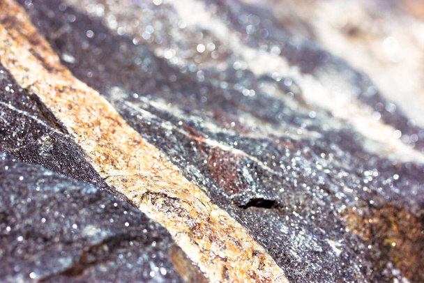 石のテクスチャを近いうちに花崗岩。侵入岩の背景。ゴールデンまたはベージュのストライプと大規模な未処理の濃い灰色の輝く石の表面。天然素材。大理石岩のマクロ写真の背景. - 写真・画像