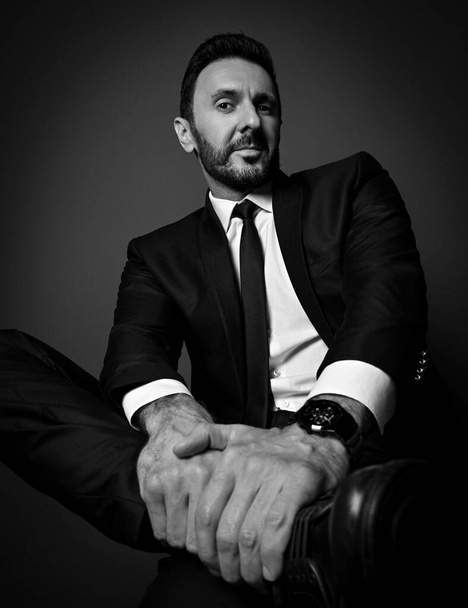 Black and white. Self-confident businessman in modern office suit sits with legs crossed looking down with interest - Photo, image