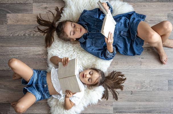Two cute children reading books lying on the floor at home. - Zdjęcie, obraz