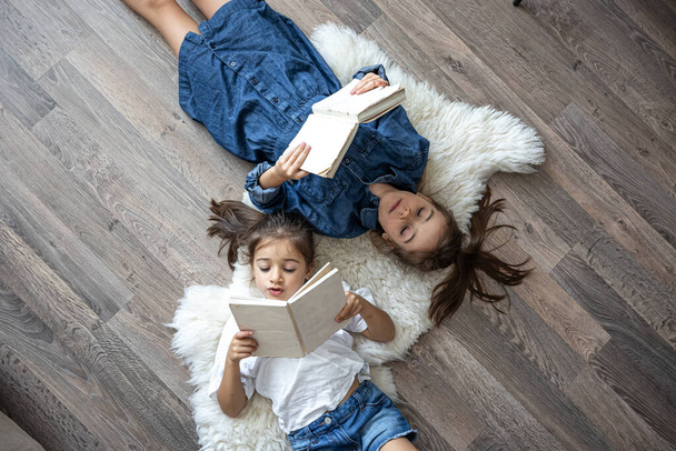 Dwoje uroczych dzieci czytających książki leżące na podłodze w domu. - Zdjęcie, obraz