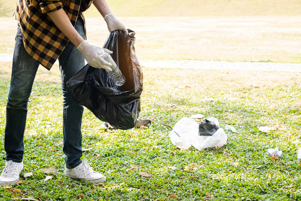 Man's hands pick up plastic bottles, put garbage in black garbage bags to clean up at parks, avoid pollution, be friendly to the environment and ecosystem. - Photo, image