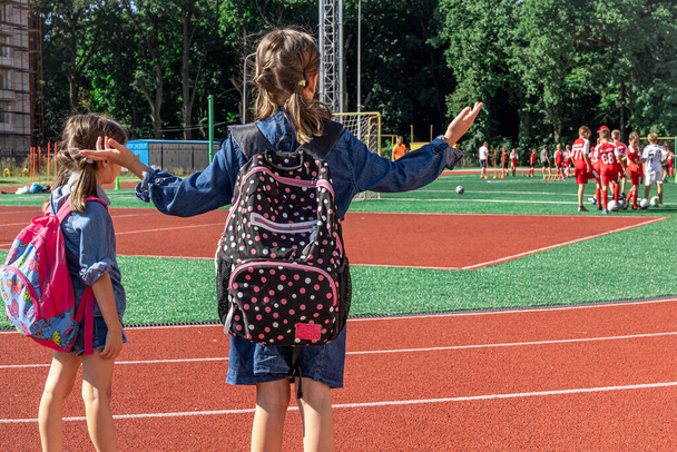 Little girls school children with backpacks in the stadium, watching the boys play football. - 写真・画像