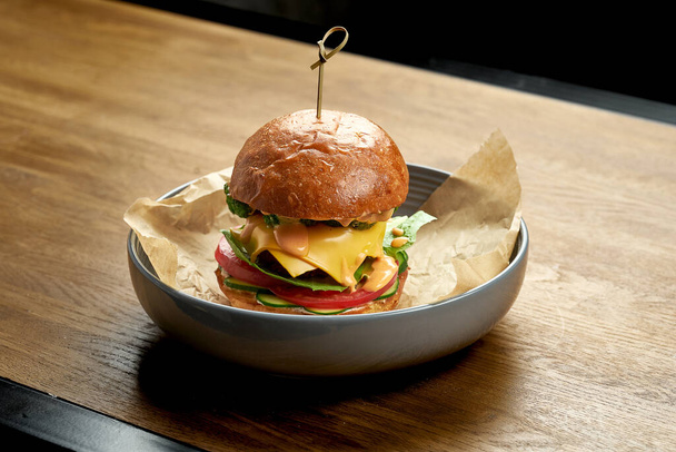 Burger with fish, melted cheese, vegetables and white sauce with brioche bun on a wooden table. - Foto, afbeelding
