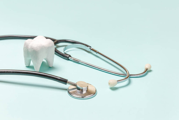 Terveydenhuollon käsite. Lääkintälaitteet stetoskooppi valkoinen terve hammas eristetty pastellin sininen tausta. Laite hammaslääkäriä varten. Suuhygienia, hammaslääkäripäivä - Valokuva, kuva