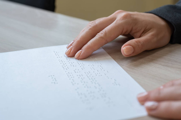 Frau in Großaufnahme liest Blinden den Text vor. Frauenhände auf Papier mit Brailleschrift. - Foto, Bild