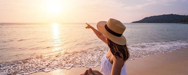 Młoda kobieta podróżnik trzymając człowieka za rękę i patrząc piękny zachód słońca na plaży, Para na wakacjach w koncepcji latem - Zdjęcie, obraz