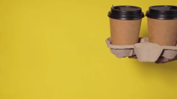 Detailní záběr na žluté pozadí, ženské ruce drží dva papírové šálky s kávou ve stojanu. Kávu nebo čaj s tebou. Propagace dvě za cenu jedné, dodání kávy na žlutém pozadí - Záběry, video