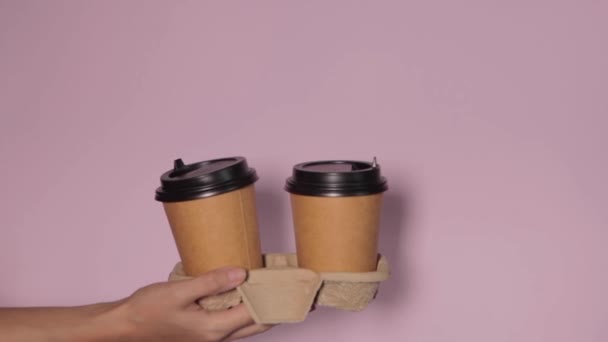 Крупним планом на рожевому тлі, рука жінки тримає паперову чашку з кавою на підставці. Кава або чай, щоб піти. Люди передають один одному чашку кави, доставку кави
. - Кадри, відео