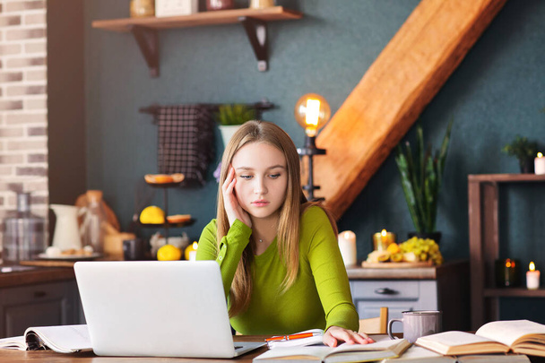 Jeune femme coûteuse pigiste assise à table à la maison avec un ordinateur portable, prenant des notes, regardant attentivement dans l'air, pensant à de nouvelles idées, blogueuse à la recherche d'inspiration. Concept freelance - Photo, image