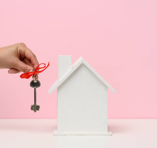 hand holds keys and wooden house on a pink background. Real estate rental, purchase and sale concept. Realtor services, building repair and maintenance, copy space - Foto, immagini