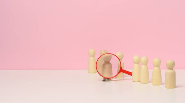 figuras de madera de los hombres de pie sobre un fondo rosa y una lupa de plástico rojo. Concepto de reclutamiento, búsqueda de empleados talentosos y capaces, crecimiento de carrera, espacio de copia - Foto, imagen
