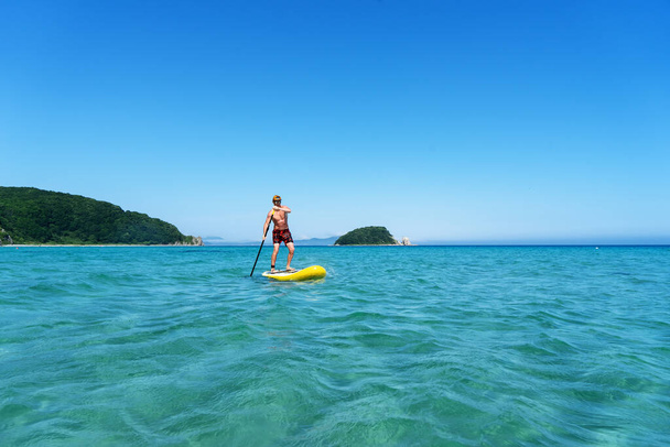 Tanned man relaxing sitting on surfboard with paddle relaxing at coast summer travel vacation - Foto, Imagem