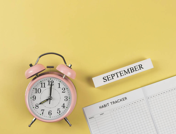 Top view or flat lay of habit tracker book, pink vintage alarm clock and wooden calendar september on yellow background. - Fotó, kép