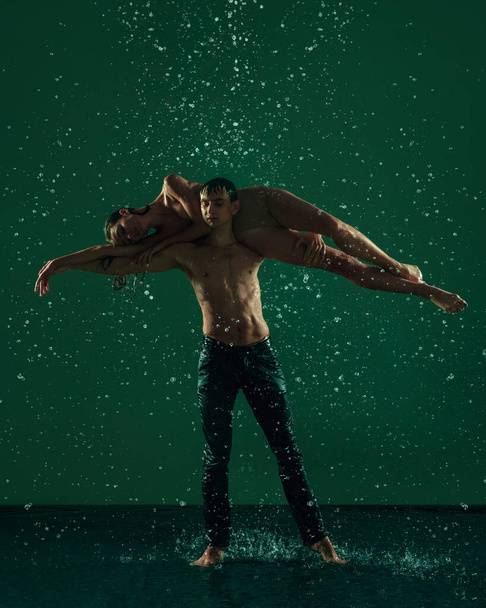 Two young ballet dancers, man and woman dancing in the raindrops over dark background. Art, action, inspiration concept. - Foto, immagini