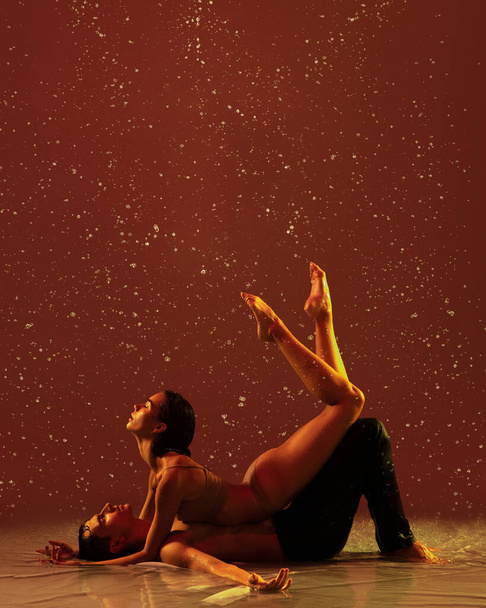 İki genç balerin, erkek ve kadın, kırmızı arka planda yağmurun altında yerde yatıyor. Aşk, sanat, ilham konsepti. - Fotoğraf, Görsel