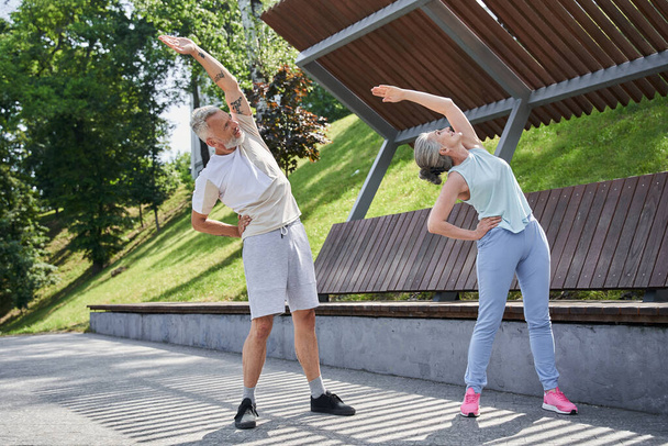 Positive senior couple are exercising jointly on the summer park - Фото, зображення