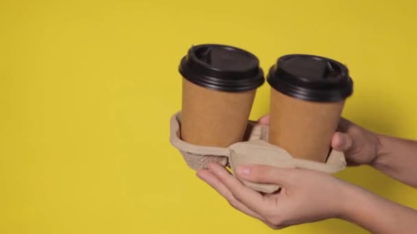 Großaufnahme auf gelbem Hintergrund, Frauenhände halten zwei Pappbecher mit Kaffee in einem Ständer. Kaffee oder Tee mit Ihnen. Aktion zwei zum Preis von einem, Kaffeelieferung auf gelbem Hintergrund - Filmmaterial, Video