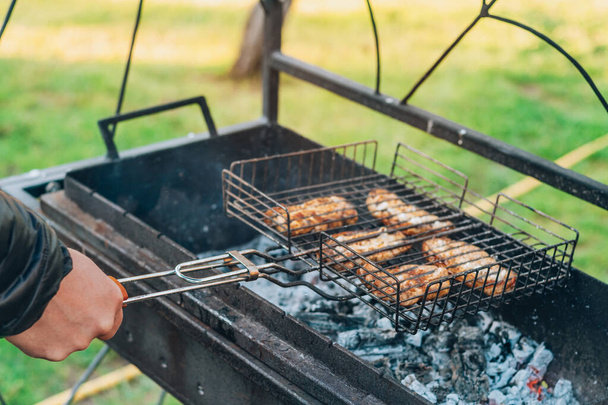 Mužská ruka mění syrové grilované kousky masa na grilu vařeném na grilu na dřevěném uhlí. Vaření BBQ venku - Fotografie, Obrázek
