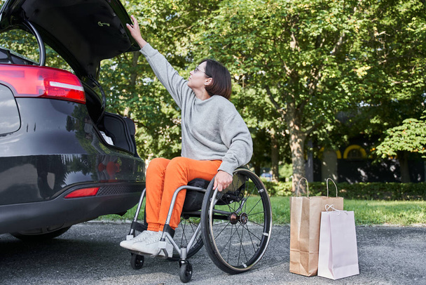 Woman at the wheelchair opening car trunk while preparing putting her purchases inside - Photo, Image