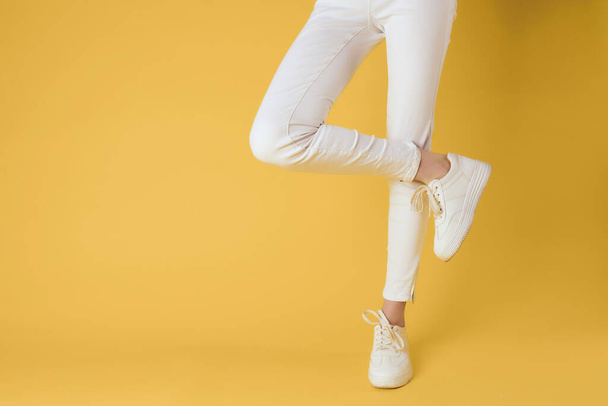 vrouwen sneakers poseren moderne stijl gele achtergrond - Foto, afbeelding