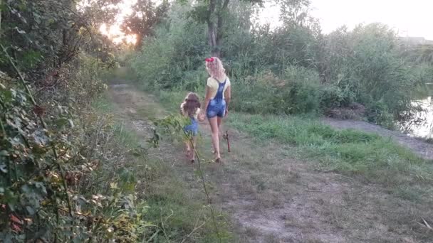 Μητέρα και κόρη πάνε για ψάρεμα ξυπόλητοι κρατώντας τα χέρια το ηλιοβασίλεμα. Μαμά με καλάμι ψαρέματος και κόρη με κουβά.. - Πλάνα, βίντεο