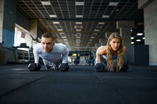 Couple faisant push-ups avec haltères dans la salle de gym - Photo, image