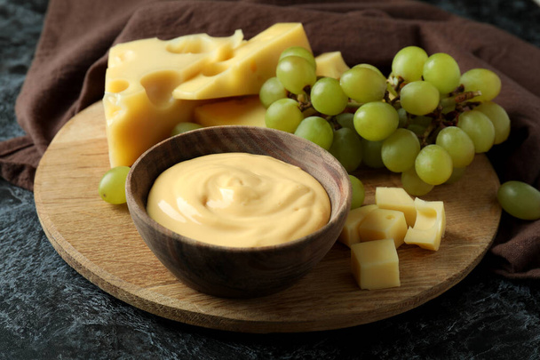 Tabuleiro com molho de queijo, uva e queijo sobre mesa de fumaça preta com toalha de cozinha - Foto, Imagem