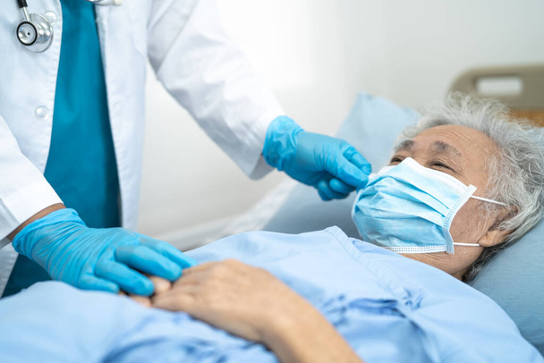 Arts helpen Aziatische senior of oudere oude dame patiënt met een gezichtsmasker in het ziekenhuis voor de bescherming van de veiligheid infectie en doden Covid-19 Coronavirus. - Foto, afbeelding