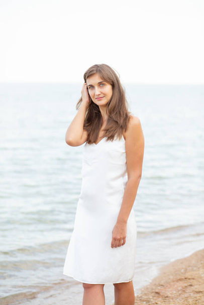 κορίτσι σε ένα λευκό φόρεμα στην παραλία κοντά στη θάλασσα, όμορφο ηλιοβασίλεμα, χαμογελαστό - Φωτογραφία, εικόνα