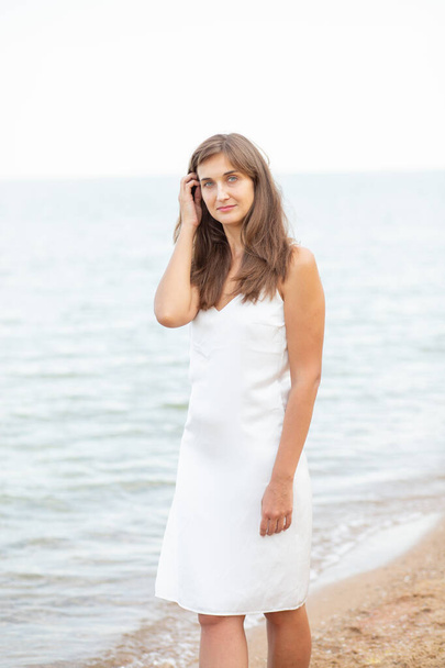 dziewczyna w białej sukience na plaży w pobliżu morza, piękny zachód słońca, uśmiech - Zdjęcie, obraz