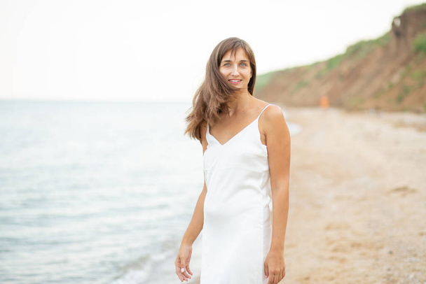 girl in a white dress on the beach near the sea, beautiful sunset, smiling - Foto, Imagem