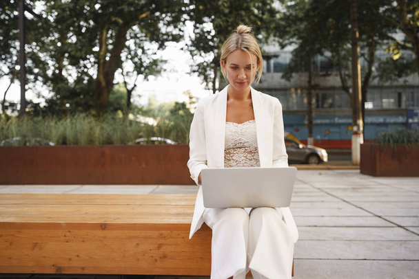 Young beautiful businesswoman working on laptop, sitting on the bench in the street - Foto, imagen