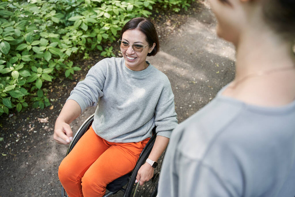 Девушка с потерей функции ноги смеется вслух, разговаривая со своей подругой в парке - Фото, изображение
