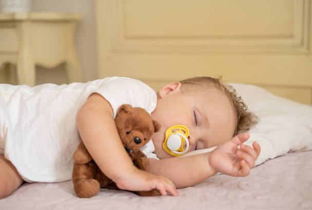 mignon bébé garçon avec mamelon dormant sur le lit à la maison. enfant étreignant ours en peluche.  - Photo, image