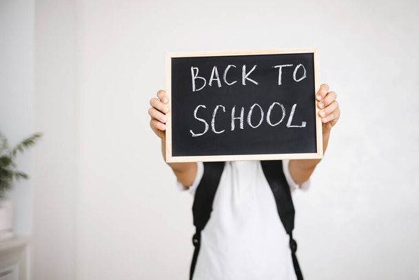 Boy with backpack holding in his hands chalk board with inscription Back to school isolated on white background - Foto, Imagem