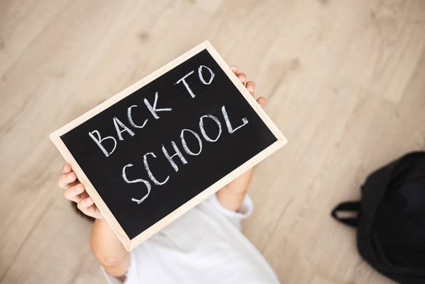 Boy with backpack holding in his hands chalk board with inscription Back to school isolated on white background - 写真・画像