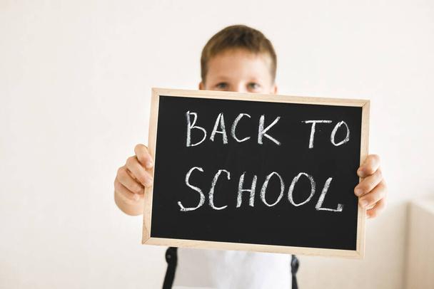 Junge mit Rucksack hält Kreidetafel mit der Aufschrift Back to school isoliert auf weißem Hintergrund in den Händen - Foto, Bild