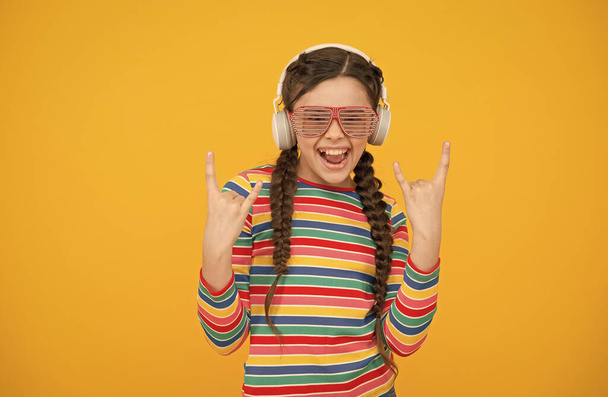 cool and hip. smiling child on yellow background. hipster party fashion style. happy teen girl wear modern headphones. funny kid listen music. beauty in glamour glasses. childhood happiness - Photo, Image