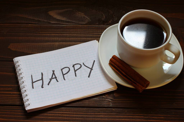Happy inscription and word in a notebook near a cup of coffee - Фото, изображение