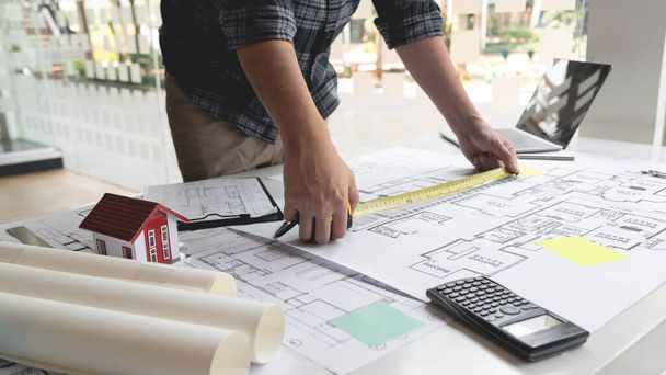 Mužský architekt používající pásku měřící a označující měřítko poměru velikostí složitého plánu. - Fotografie, Obrázek