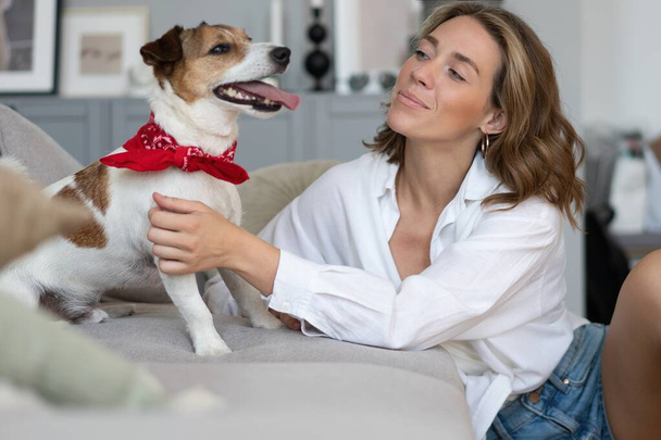 Młoda kobieta i jej pies na kanapie w domu. Uroczy zwierzak. - Zdjęcie, obraz