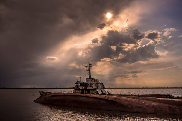 Abandoned ship in the water with a dramatic sky with sun behind the clouds in Villa Paranacito, Paran River, Entre Ros, Argentina - Photo, Image