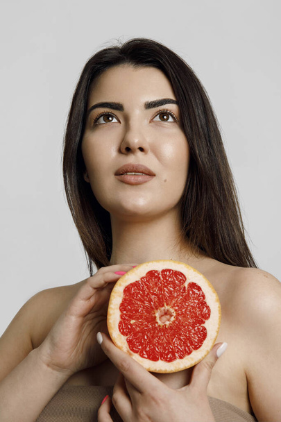Close up beauty portrait of a young woman with perfect skin with natural make up hold grapefruit isolated on beige background studio portrait. - Photo, image