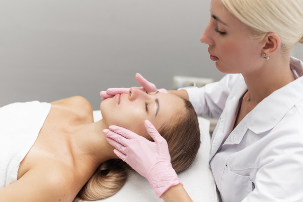 Young beautician or dermatologist doing manual facial cleansing for a woman in a beauty salon. Spa facial massage. Beautiful woman receiving facial massage in a beauty salon. The beautician makes - Zdjęcie, obraz