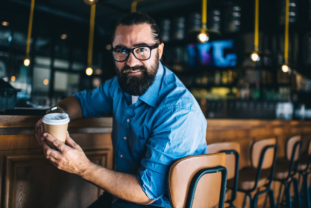 Portrait of smiling caucasian bearded man enjoying coffee break and free time looking at camera, prosperous mature 40s man owner of small business sitting at car in cafe interior enjoy job - 写真・画像