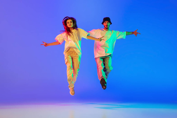 Two young people, guy and girl in casual clothes dancing contemporary dance, hip-hop over blue background in neon light. - Photo, Image